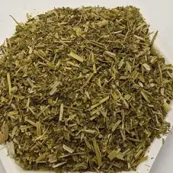Pile of dried green herb pieces, loose and chopped, on a white surface (herbal tea or seasoning herb).